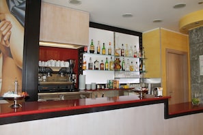 Un espace bar avec un comptoir, des étagères remplies de bouteilles d’alcool, une machine à café et une grande affiche accrochée au mur.