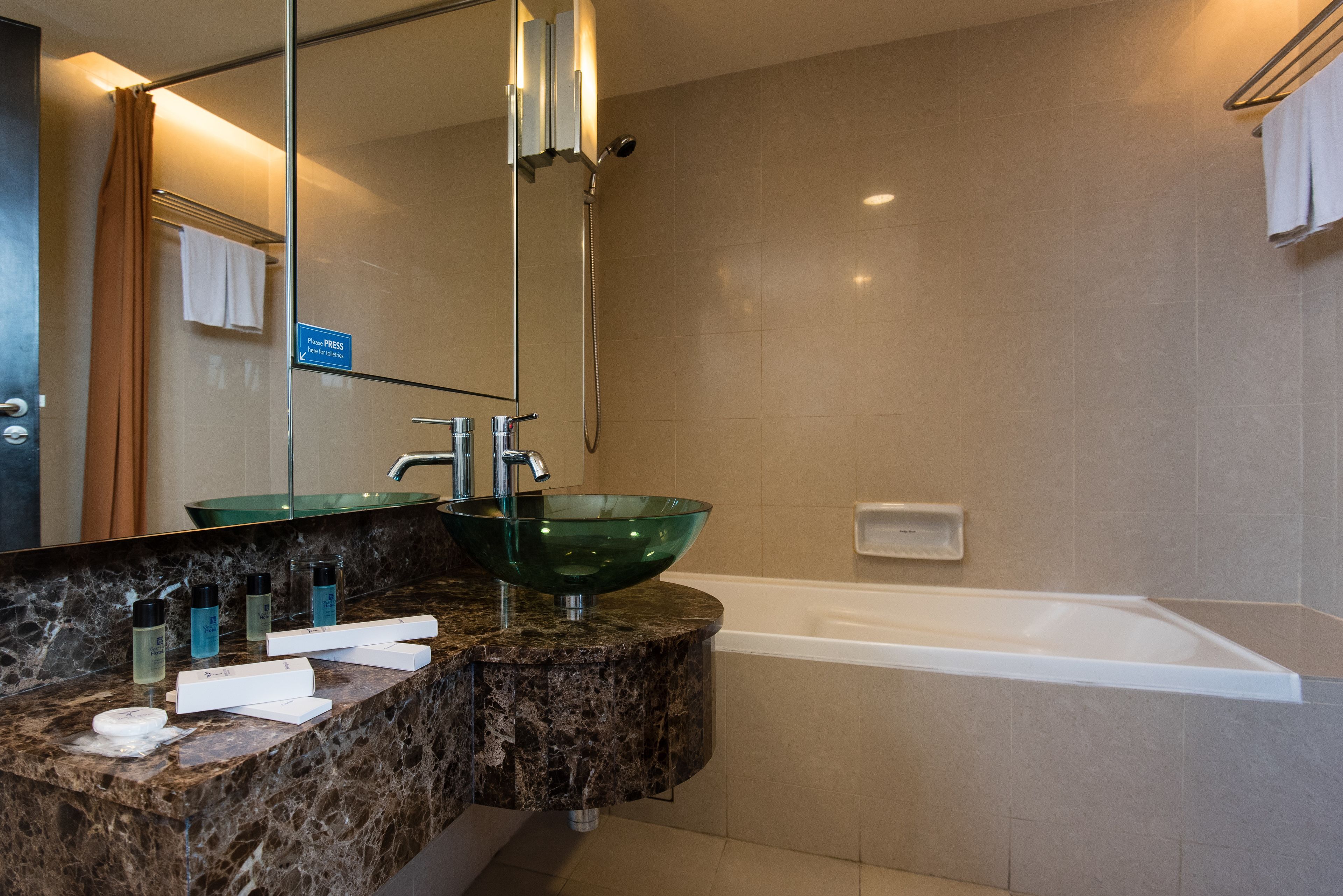 A bathroom with a glass bowl sink, a bathtub, and a vanity with toiletries.