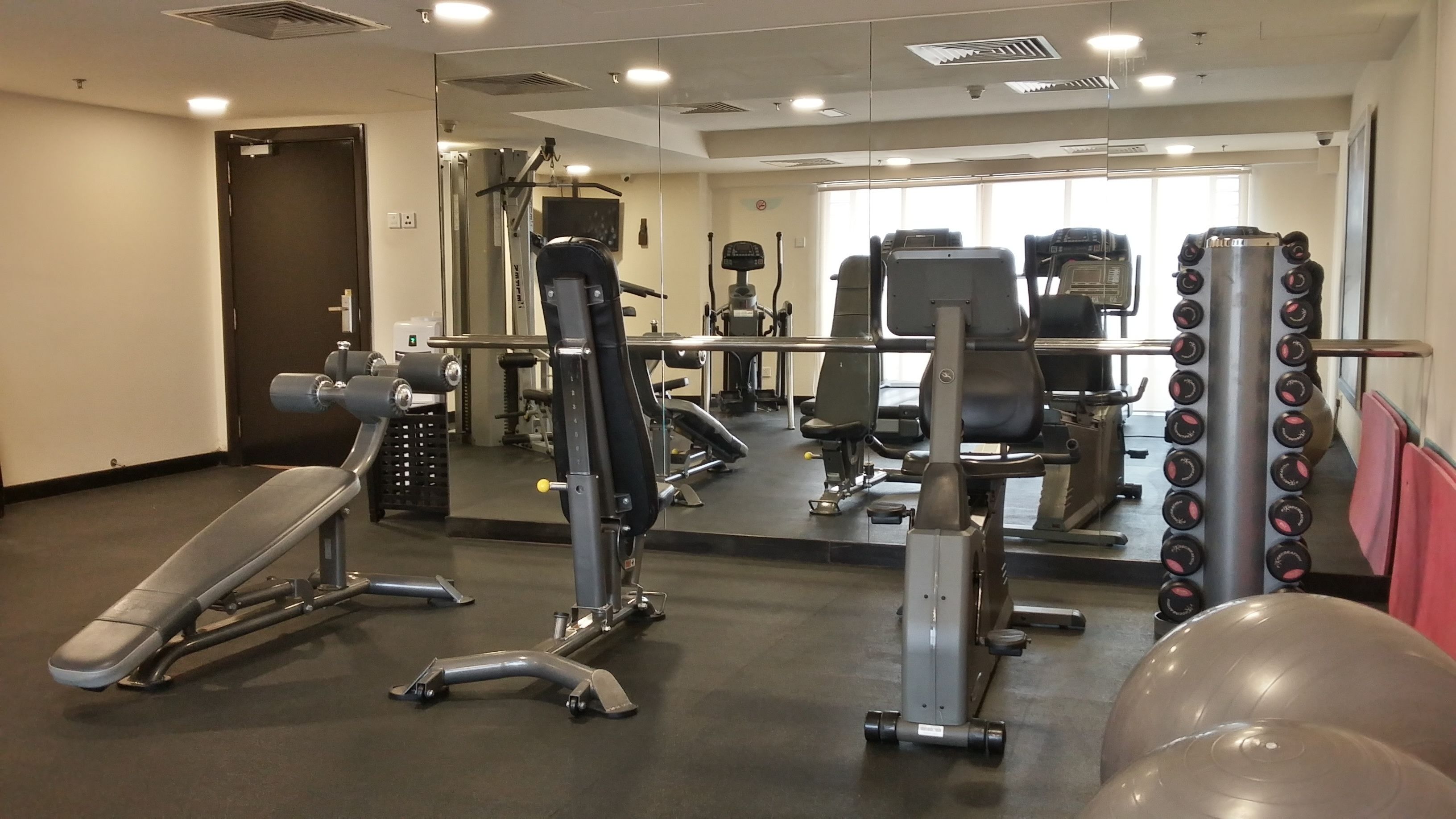 Un gimnasio con equipo de ejercicio diverso, una banca y un muro con espejos.