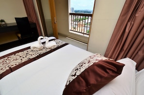 A hotel room with a bed, a desk, and a view of a cityscape through a window.