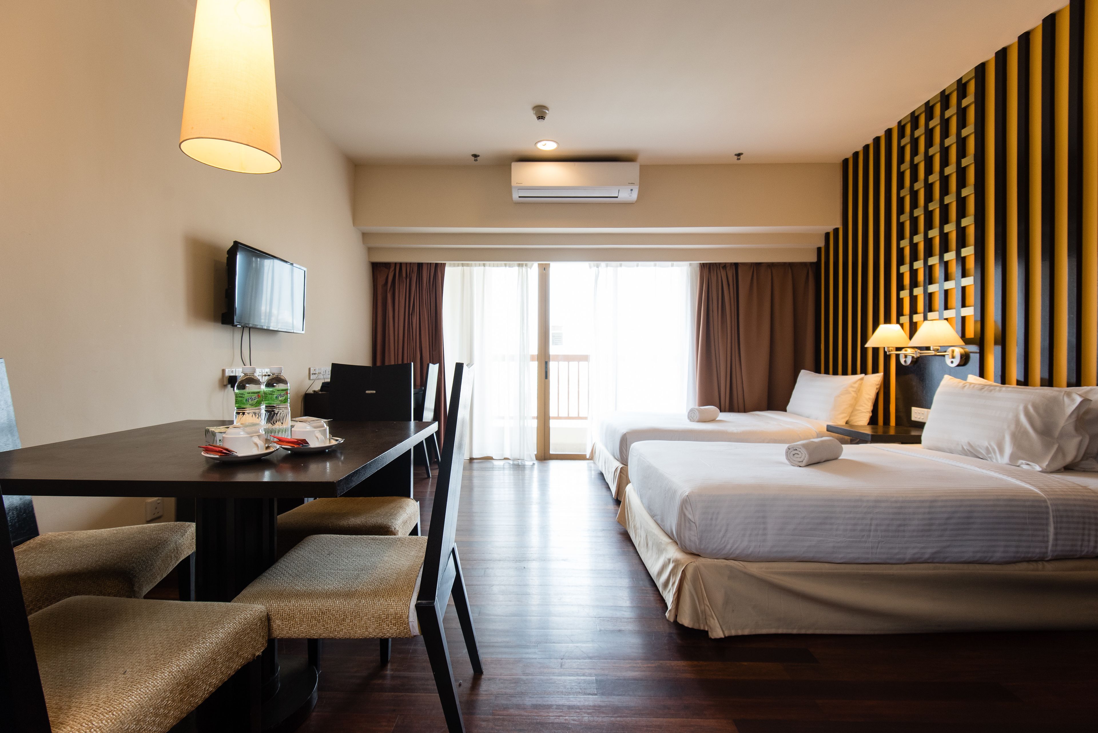 A hotel room with a desk, two beds, a TV, and a large window with curtains.