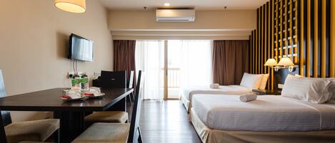 A hotel room with a desk, two beds, a TV, and a large window with curtains.