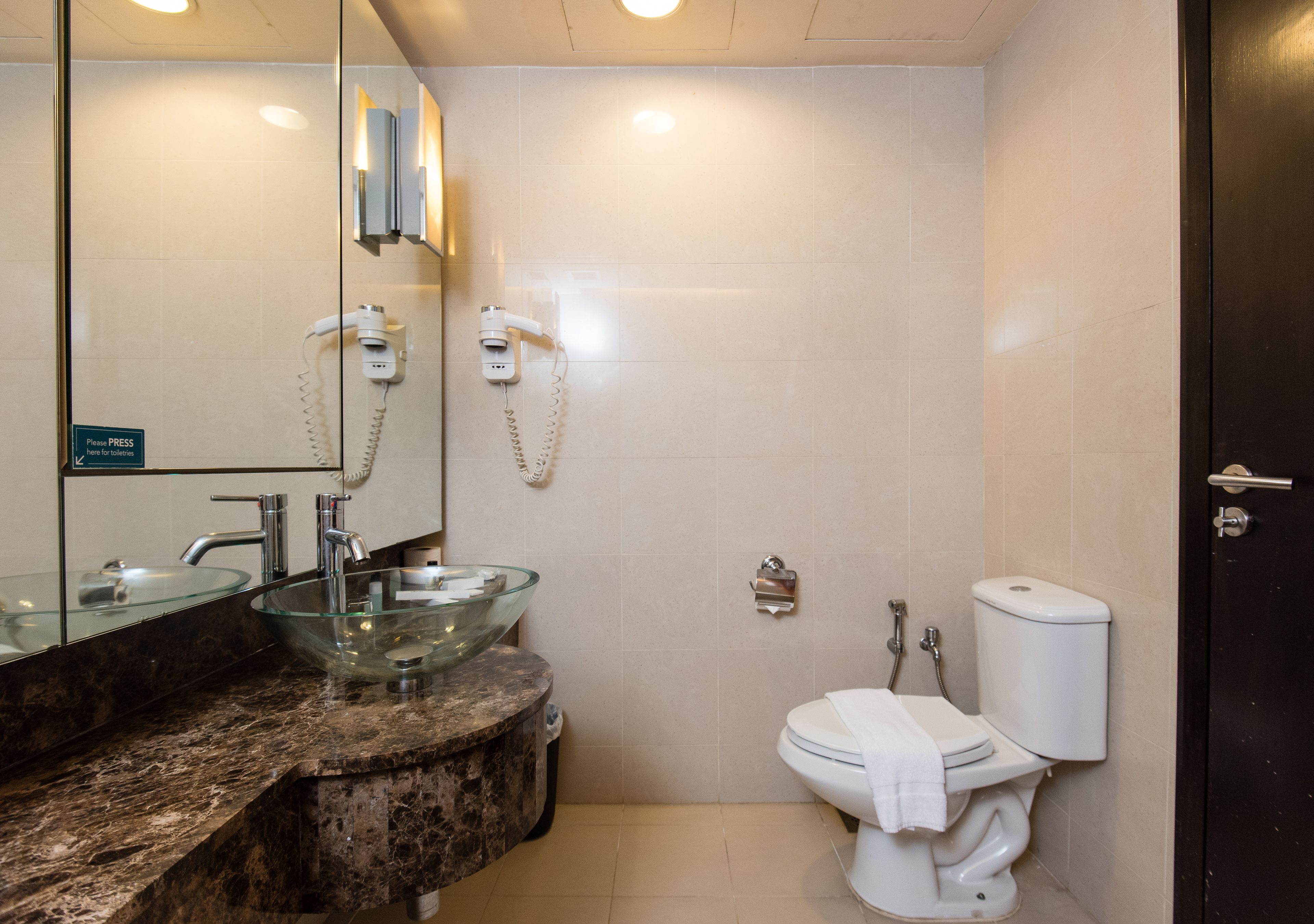 A bathroom with a glass bowl sink, a marble countertop, a toilet, and a mirror.