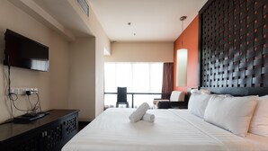 Quarto de hotel com uma cama grande, uma televisão de tela plana na parede e vista para o exterior através de uma janela ampla.
