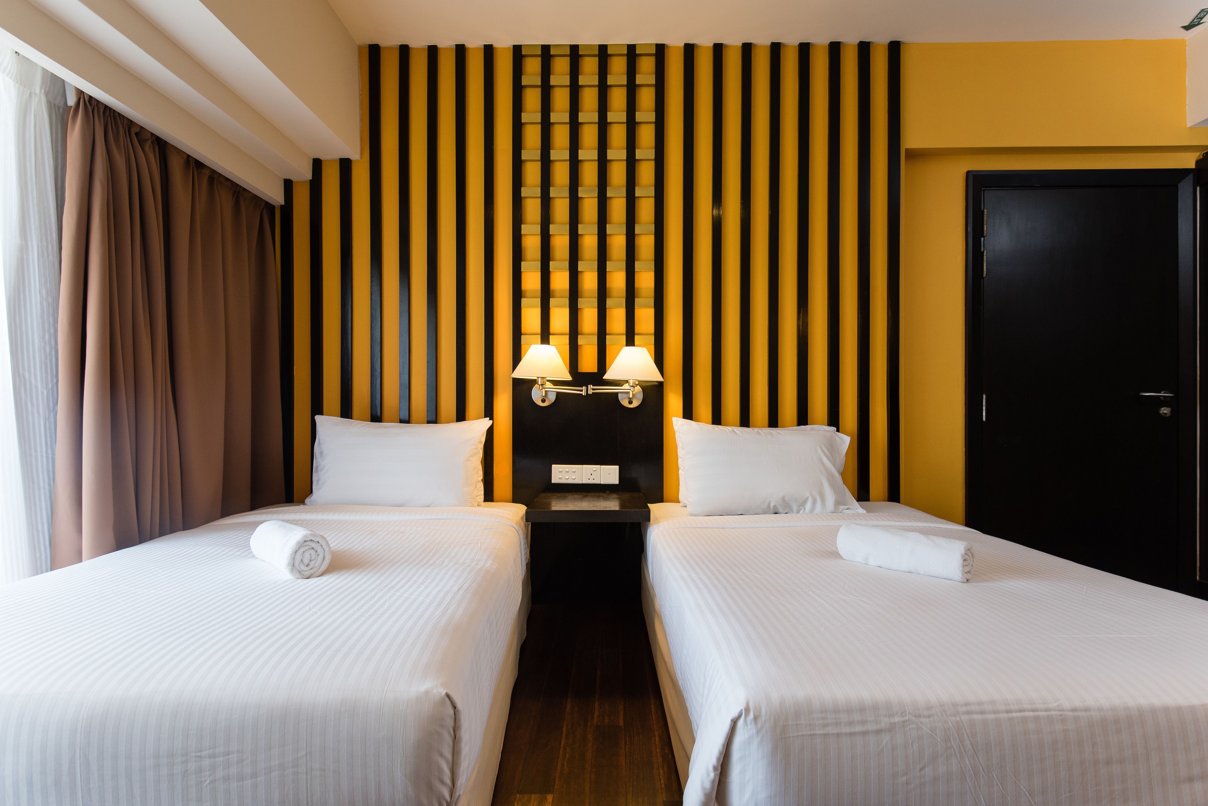 A hotel room with two beds, a black headboard with vertical stripes, and a black door.