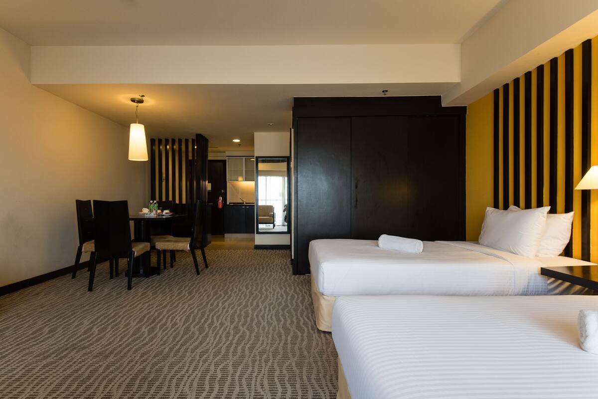 A hotel room with two beds, a desk, and a chair. There is a bathroom visible in the background.