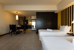A hotel room with two beds, a desk, and a chair. There is a bathroom visible in the background.