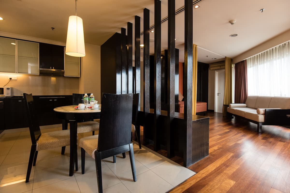 A modern living room with a sofa, a dining area with a table and chairs, and a kitchen area with cabinets and a microwave.