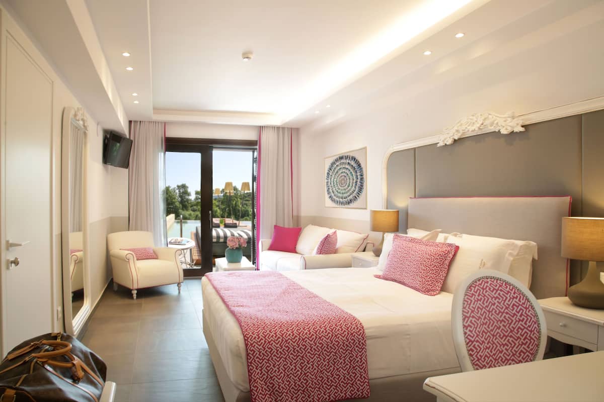 A hotel room with a large bed, a sofa, a chair, a TV, and a balcony with a view.