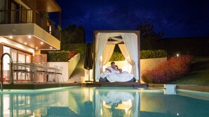 A poolside area with a canopy bed, a dining area with chairs and a table, and a staircase leading to a balcony. - Avaton Luxury Beach Resort - Relais & Chateaux (Aristotelis)