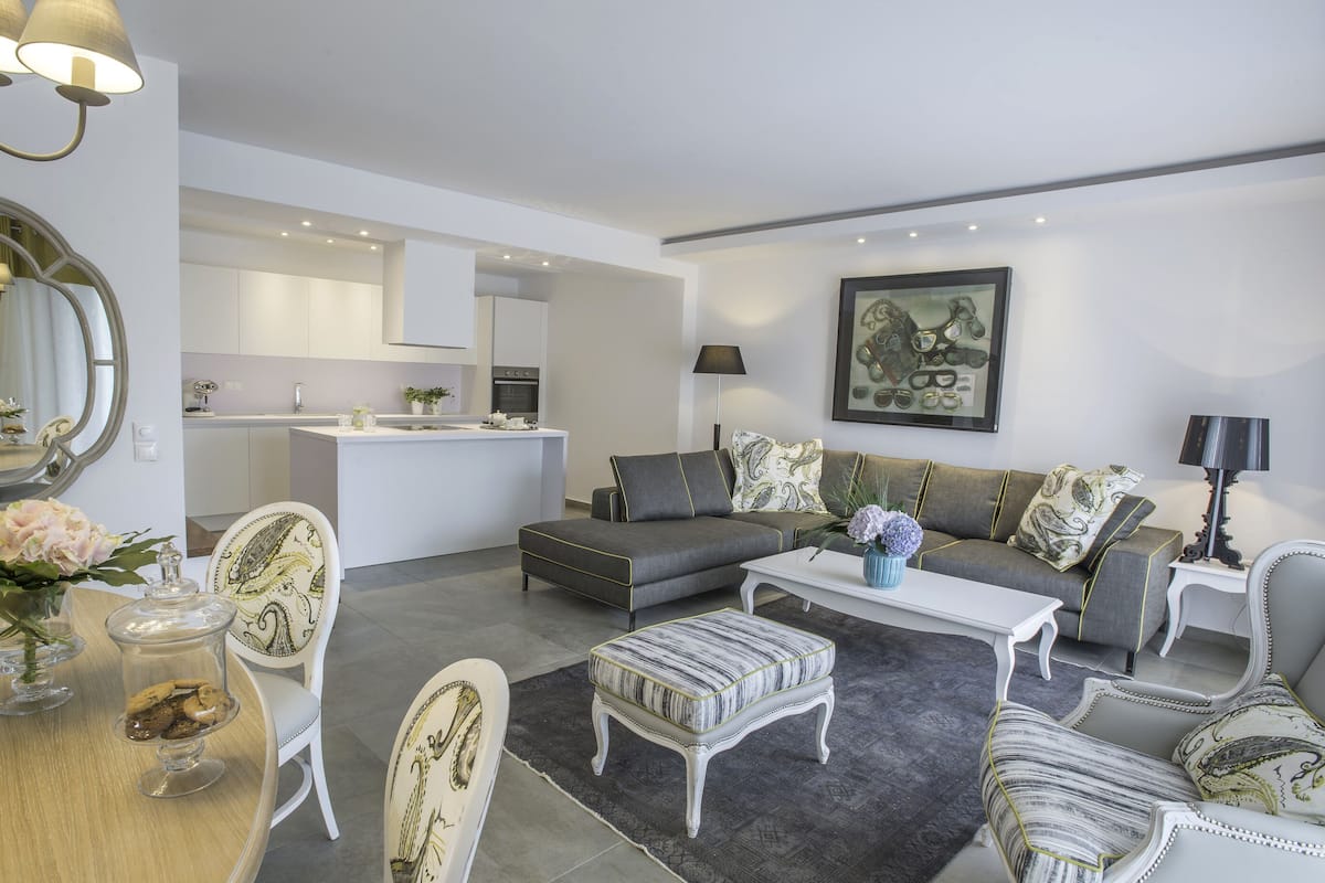 A modern living room with a grey sofa, white armchairs, a coffee table, and a dining area with a glass-top table and chairs.
