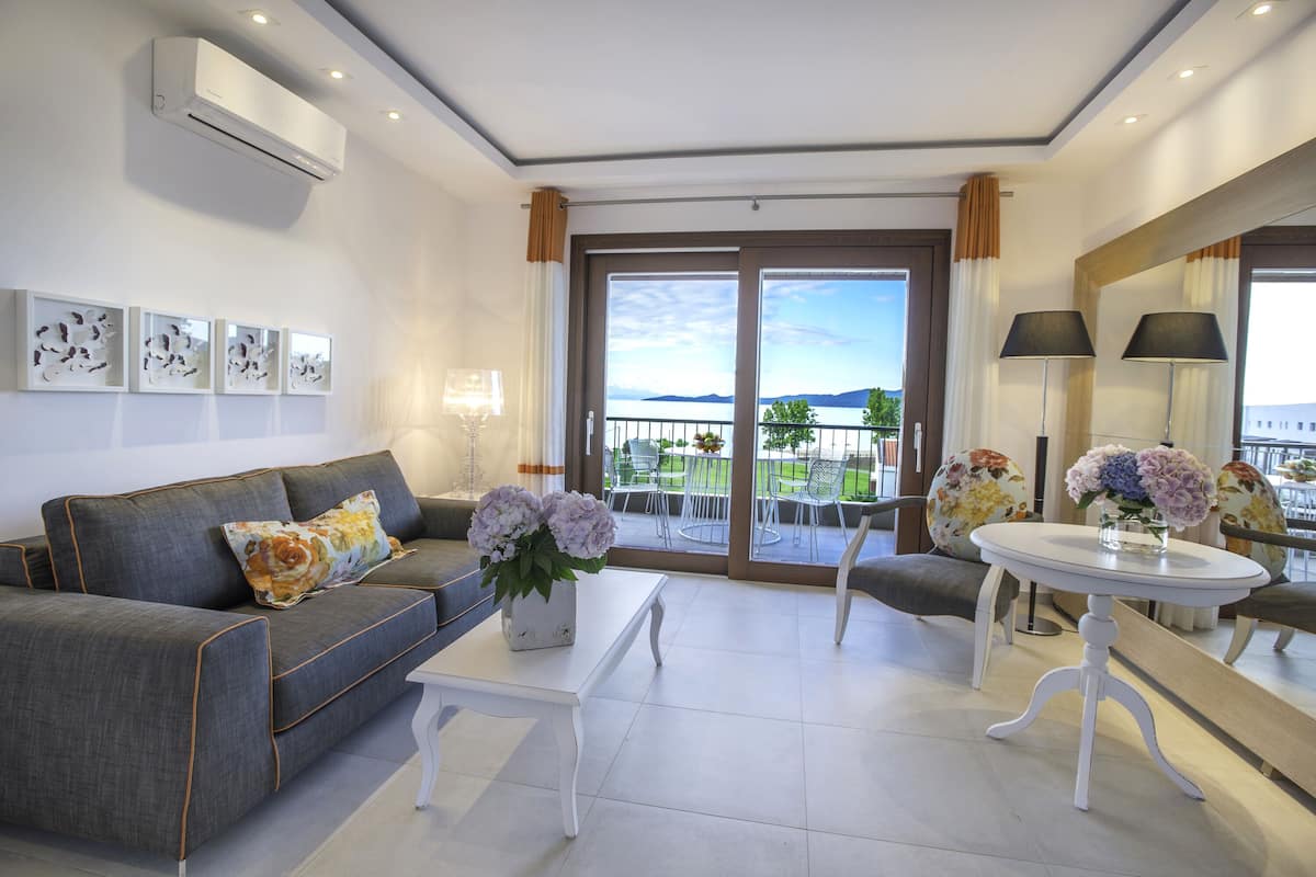 A modern living room with a grey sofa, a white coffee table, and a balcony with outdoor seating.