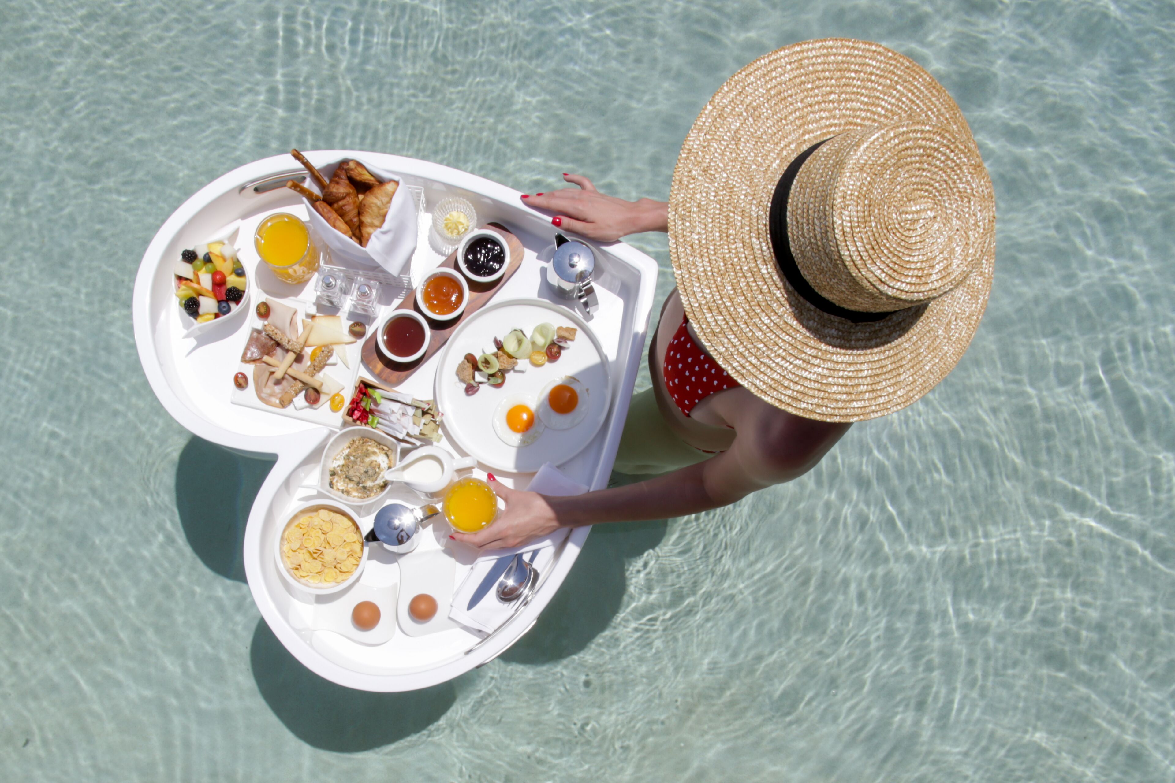 A person holding a tray with various food items and drinks, likely on a boat or near water.