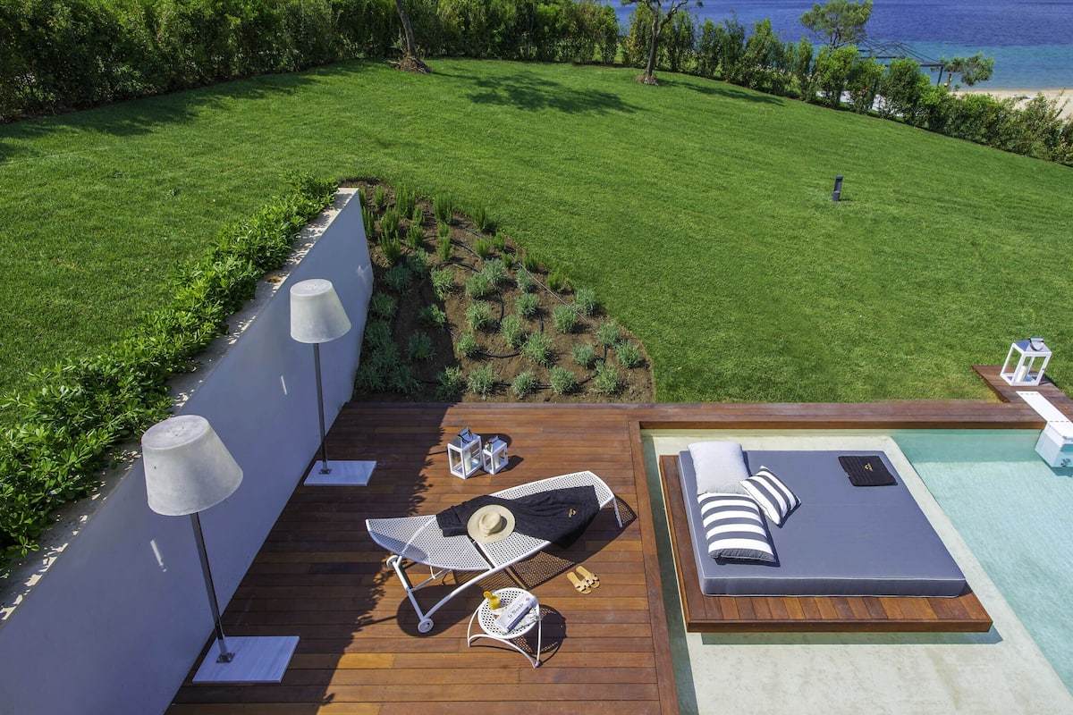 A deck with a pool, lounge chairs, and a small table with a hat and bottle.