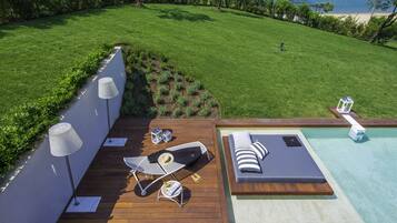 A deck with a pool, lounge chairs, and a small table with a hat and bottle.