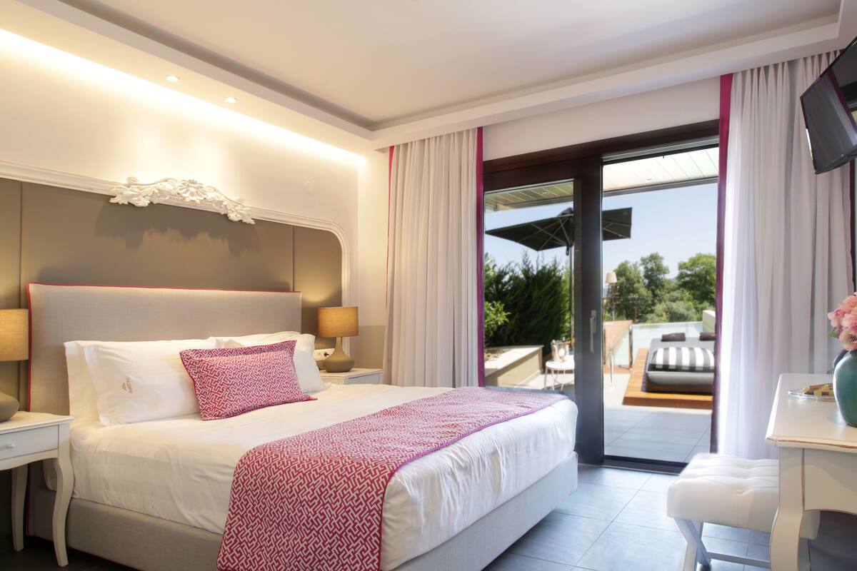 A modern hotel room with a large bed, a desk, and a balcony with outdoor seating.