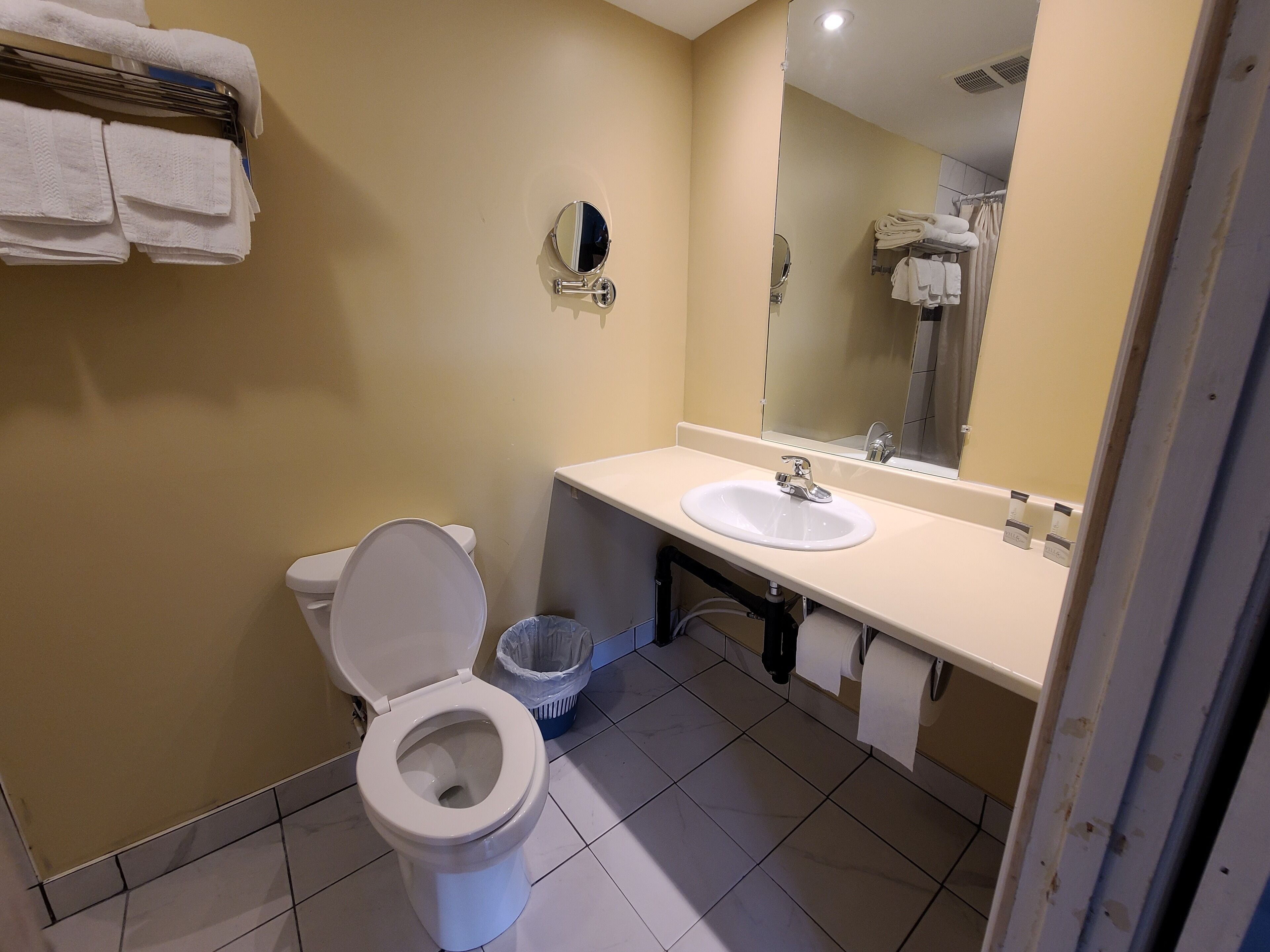 Un baño con inodoro, lavamanos, espejo y toallero.
