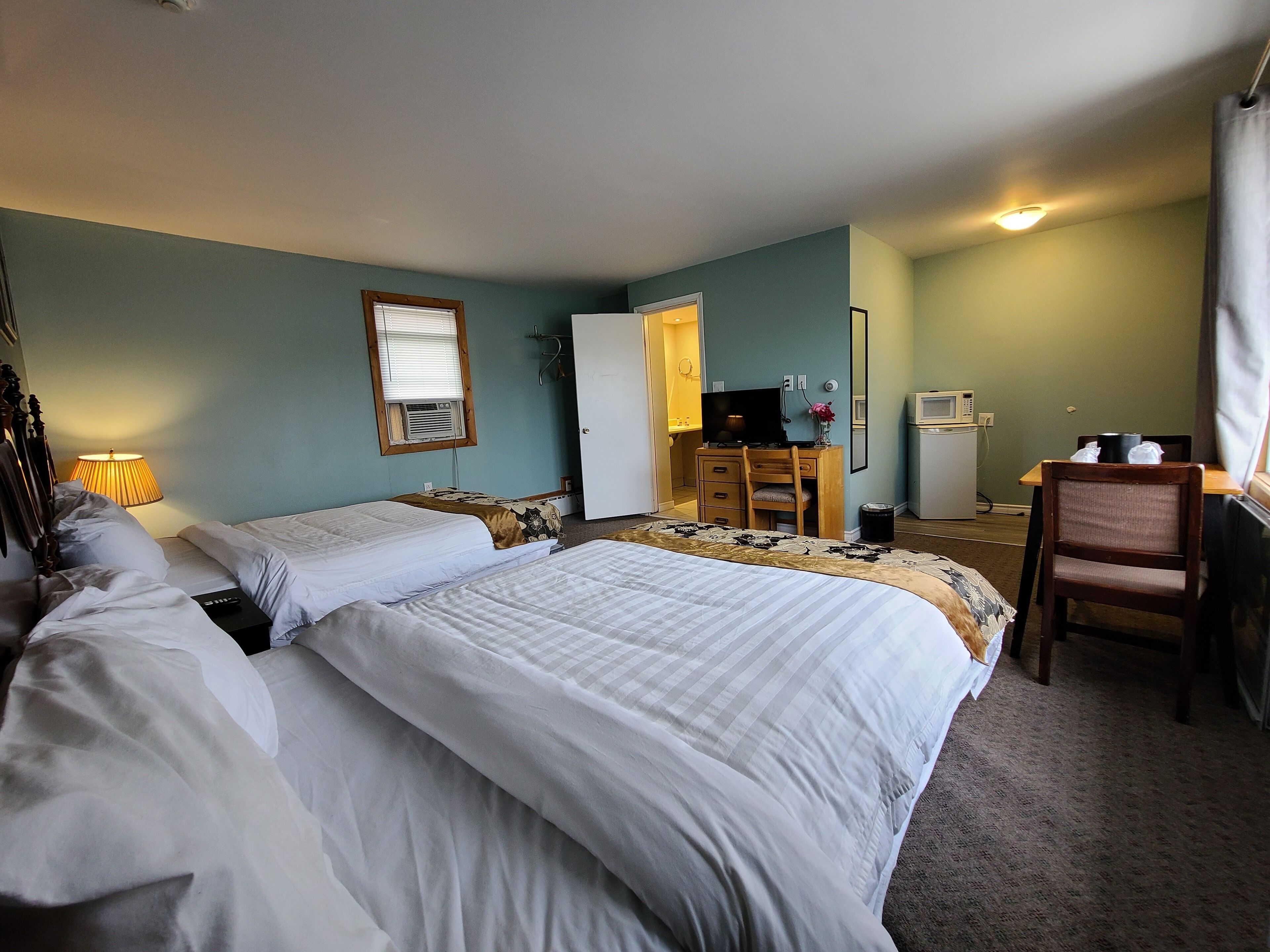 Ett hotellrum med två sängar, ett skrivbord, en stol, en TV och ett litet pentry.