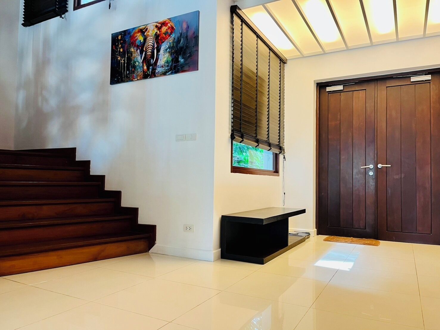 A modern interior with a wooden staircase, a painting, a window with blinds, and a closed door.