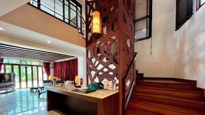 A modern hotel lobby with a reception desk, a staircase, and a large window offering a view of greenery. - Amatapura Beach Villa 15 (Krabi)
