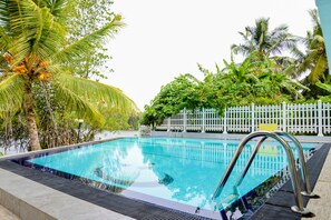 A swimming pool with a metal ladder, surrounded by lush greenery and a white picket fence.