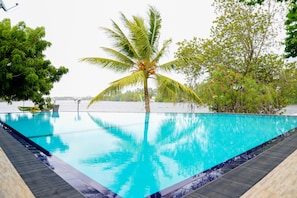 A clear blue pool with a palm tree in the center, surrounded by lush greenery and a view of the sea. - Laluna Ayurveda Resort (Aluthgama)