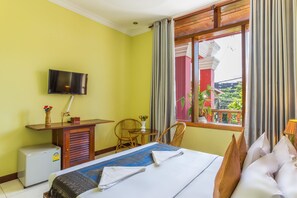 A hotel room with a bed, a television mounted on the wall, a small table with a vase of flowers, and a window with curtains. - Side Walk Never Die (Siem Reap)