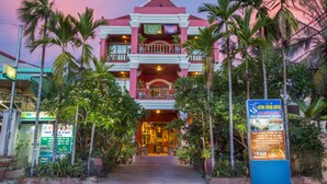 A hotel with a red facade, multiple balconies, and a signboard in front. - Side Walk Never Die (Siem Reap)