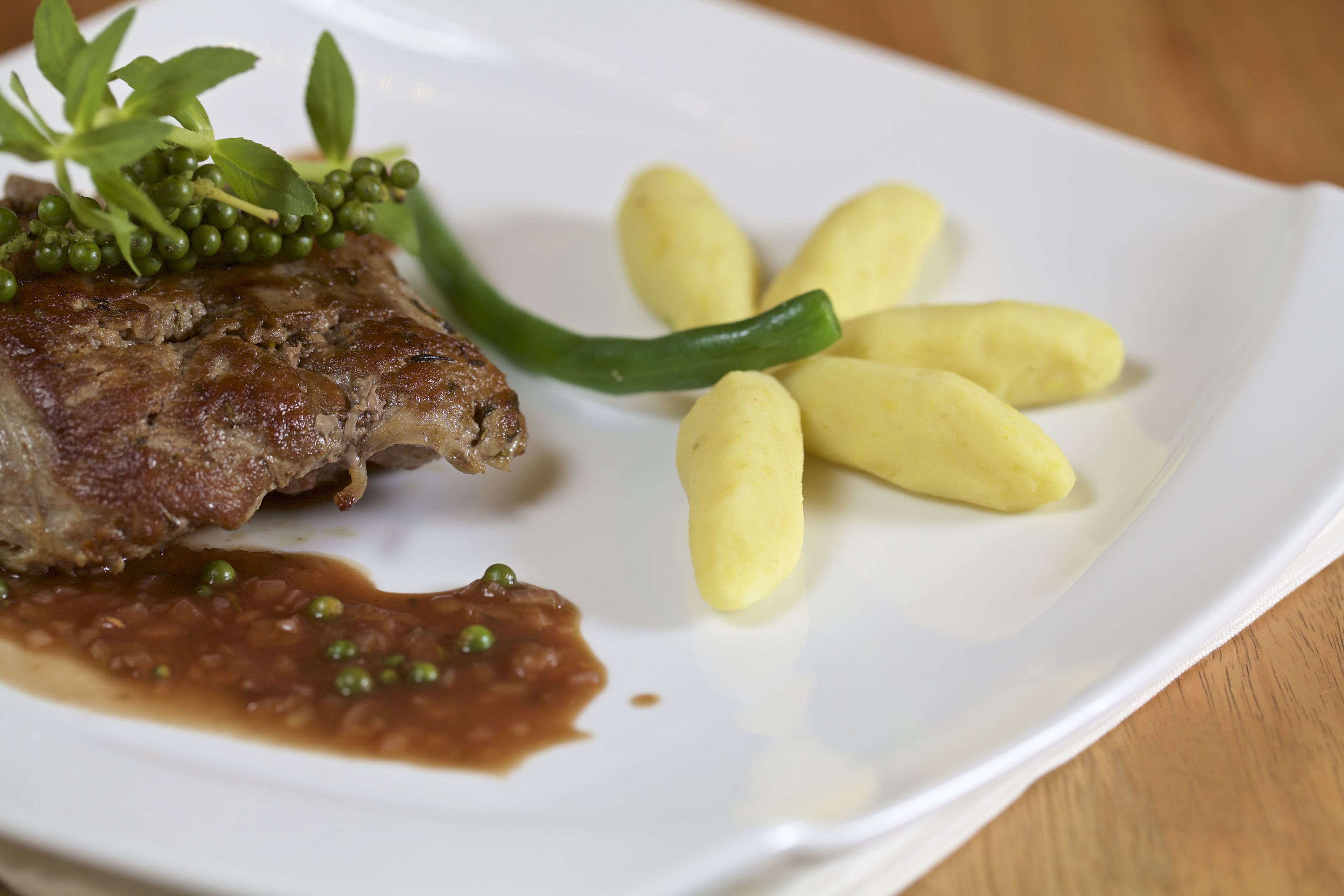 Un piatto con carne, piselli verdi, un peperoncino verde e gnocchi gialli.