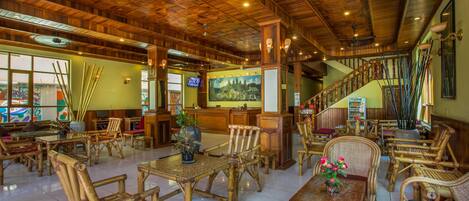 A spacious lobby with wooden furniture, a staircase, and a large painting on the wall.