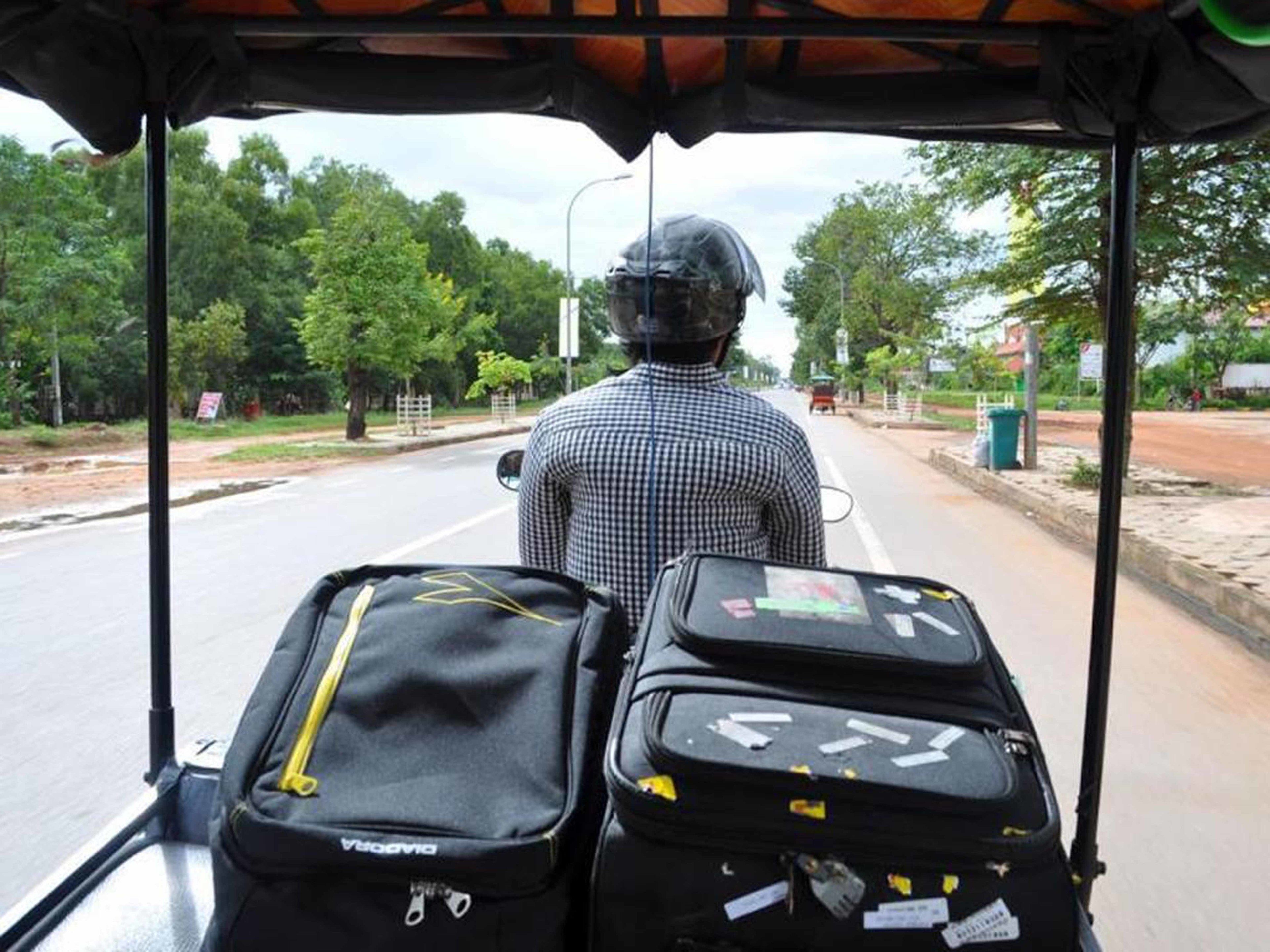 A person seated in a vehicle with luggage, looking at a road with trees and a clear sky.