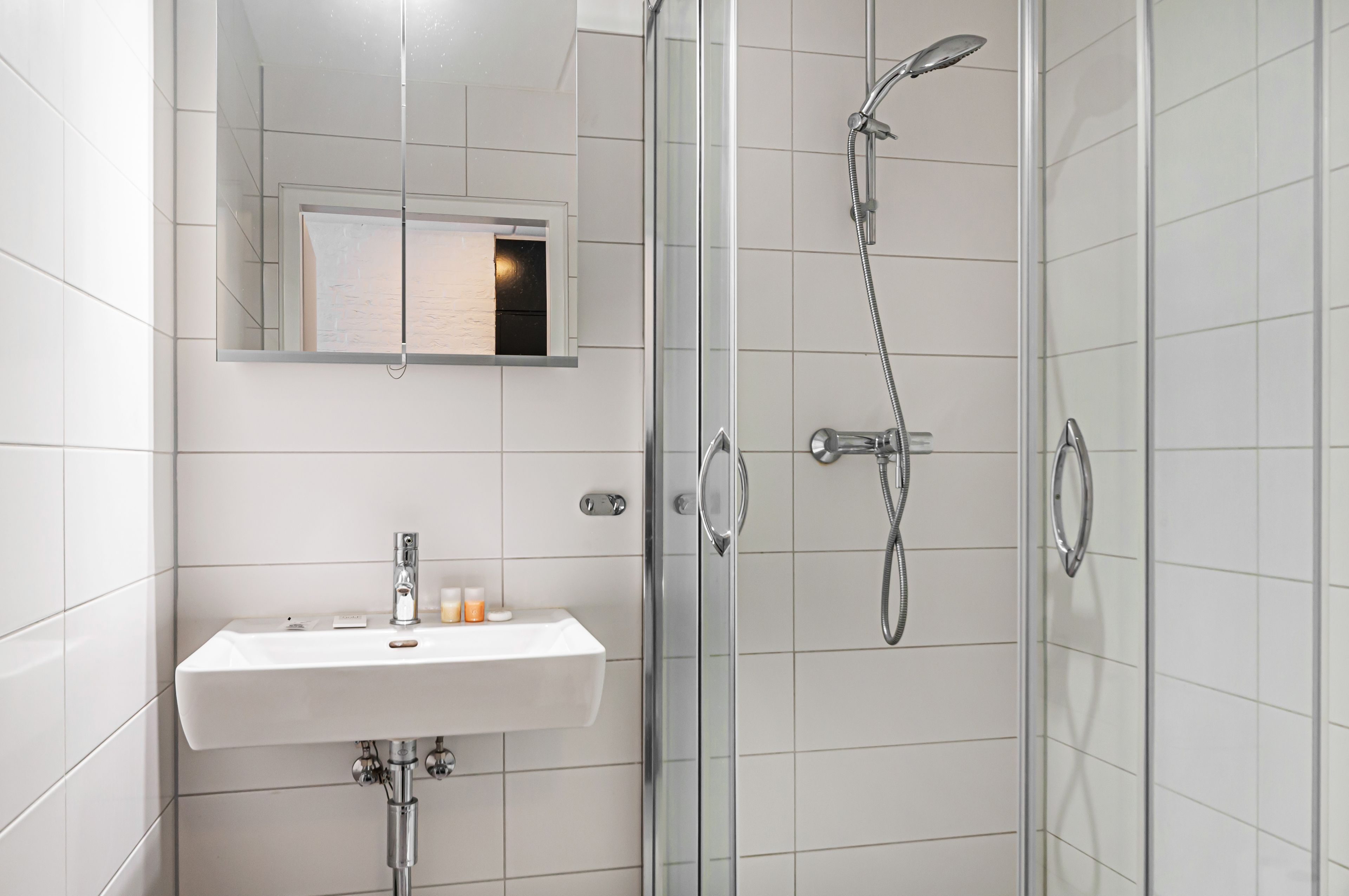 A modern bathroom with a glass-enclosed shower, a white sink with toiletries, and a mirror above the sink.