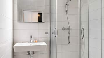 A modern bathroom with a glass-enclosed shower, a white sink with toiletries, and a mirror above the sink.