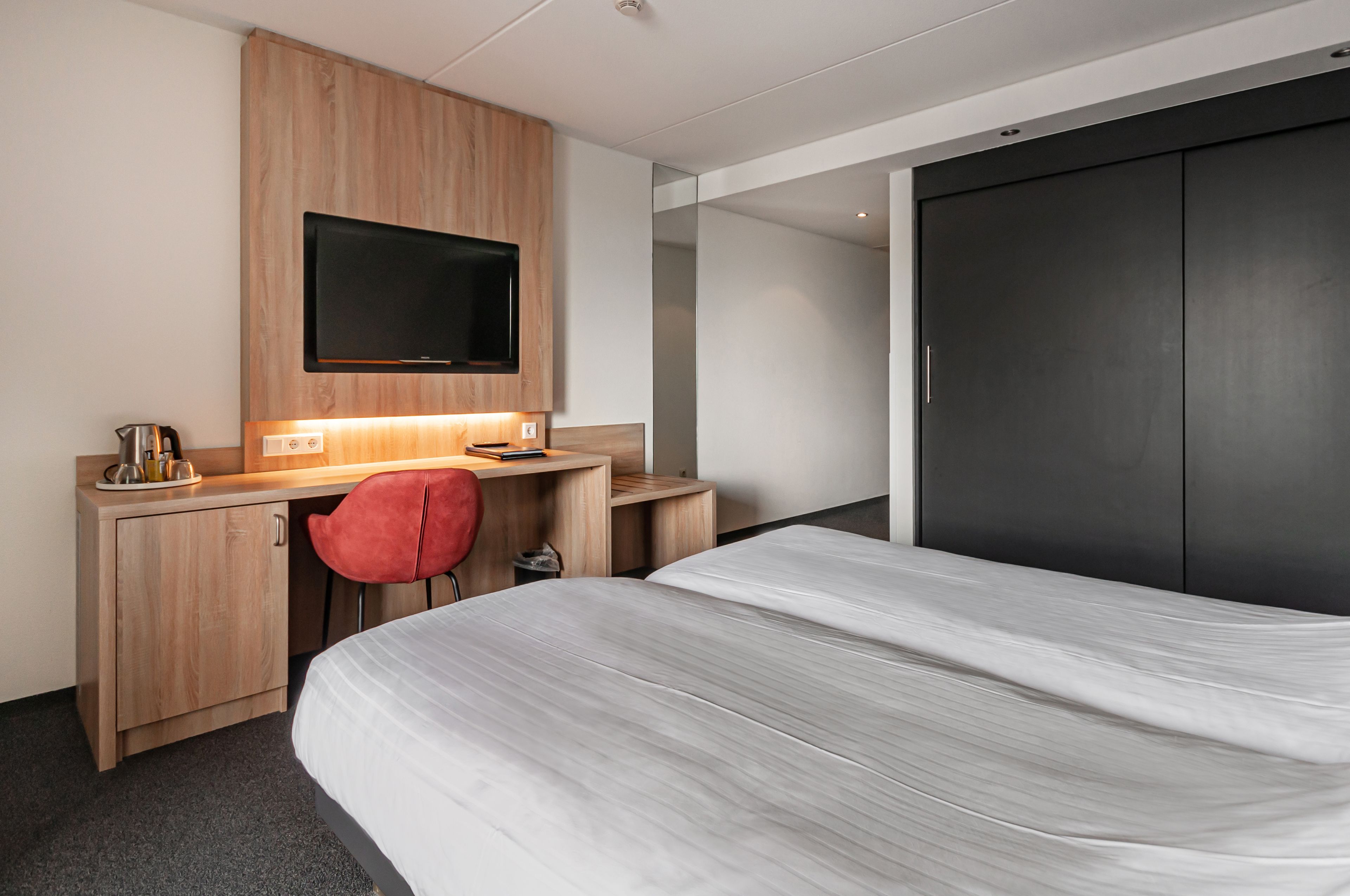 A hotel room with a bed, a desk with a chair, a television, and a wardrobe.