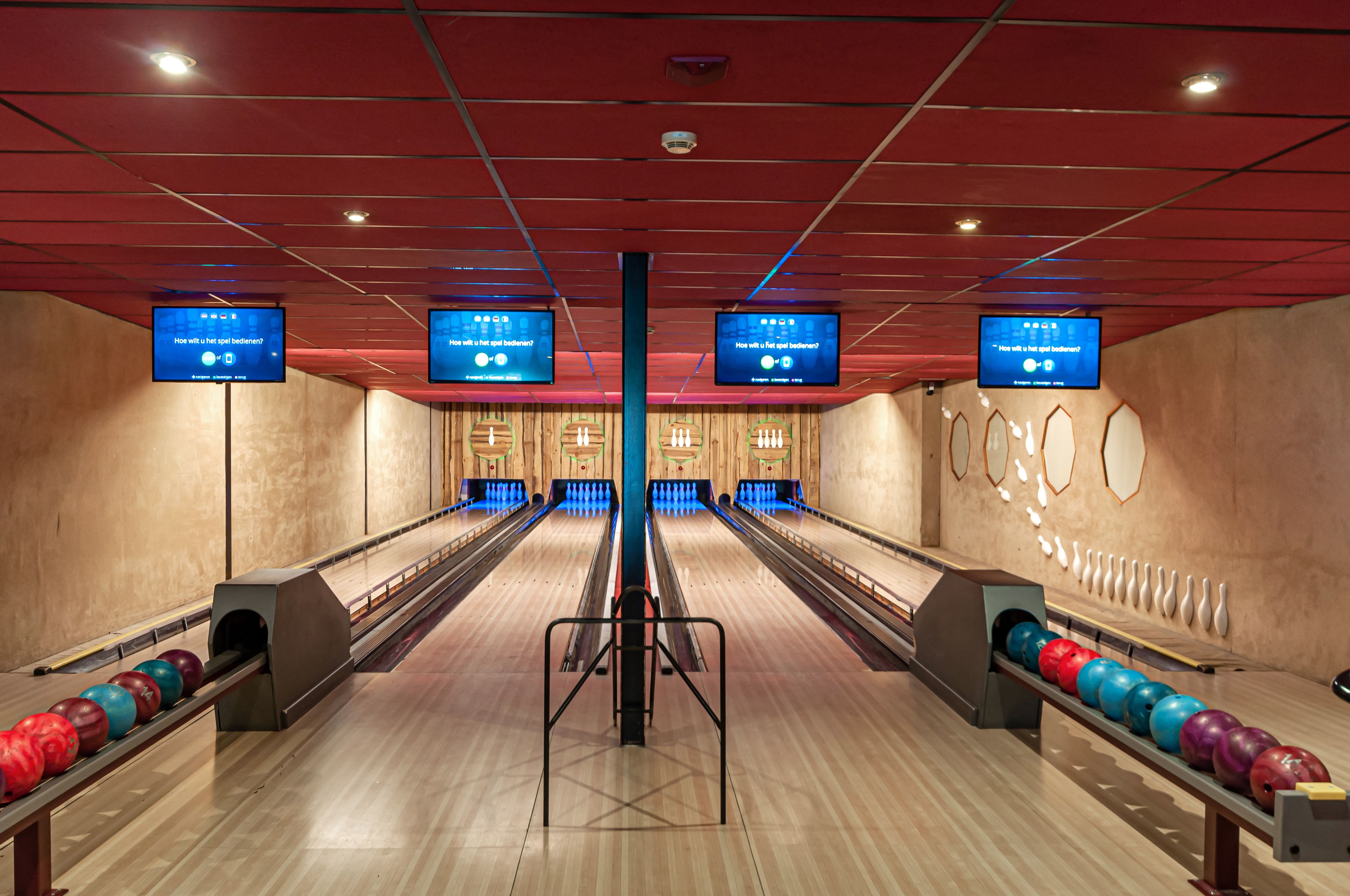 A bowling alley with multiple lanes, bowling pins, and overhead screens displaying text.