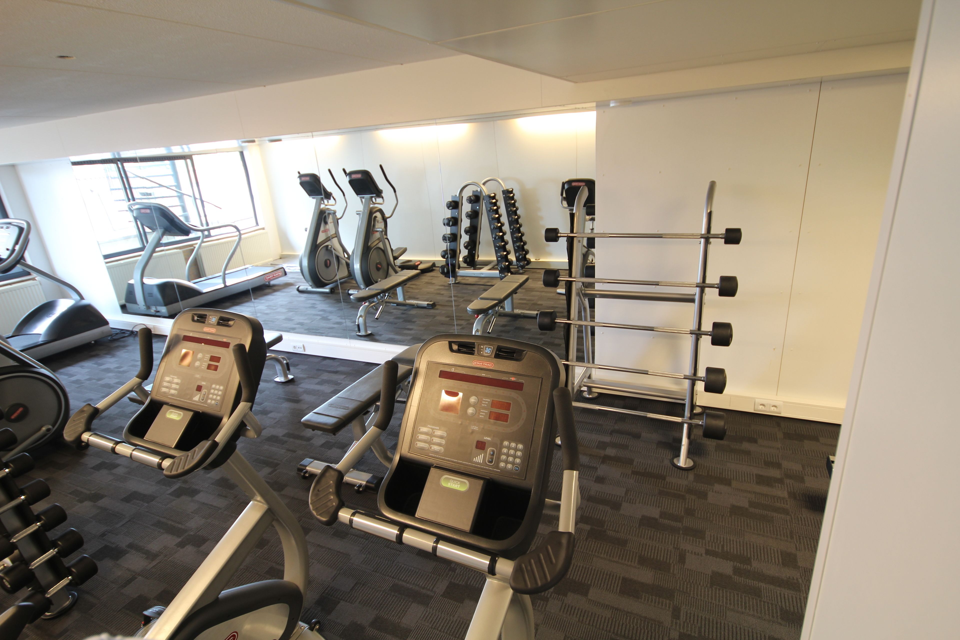 Ein Fitnessraum mit Laufbändern, Crosstrainern und einem Gewichtständer.