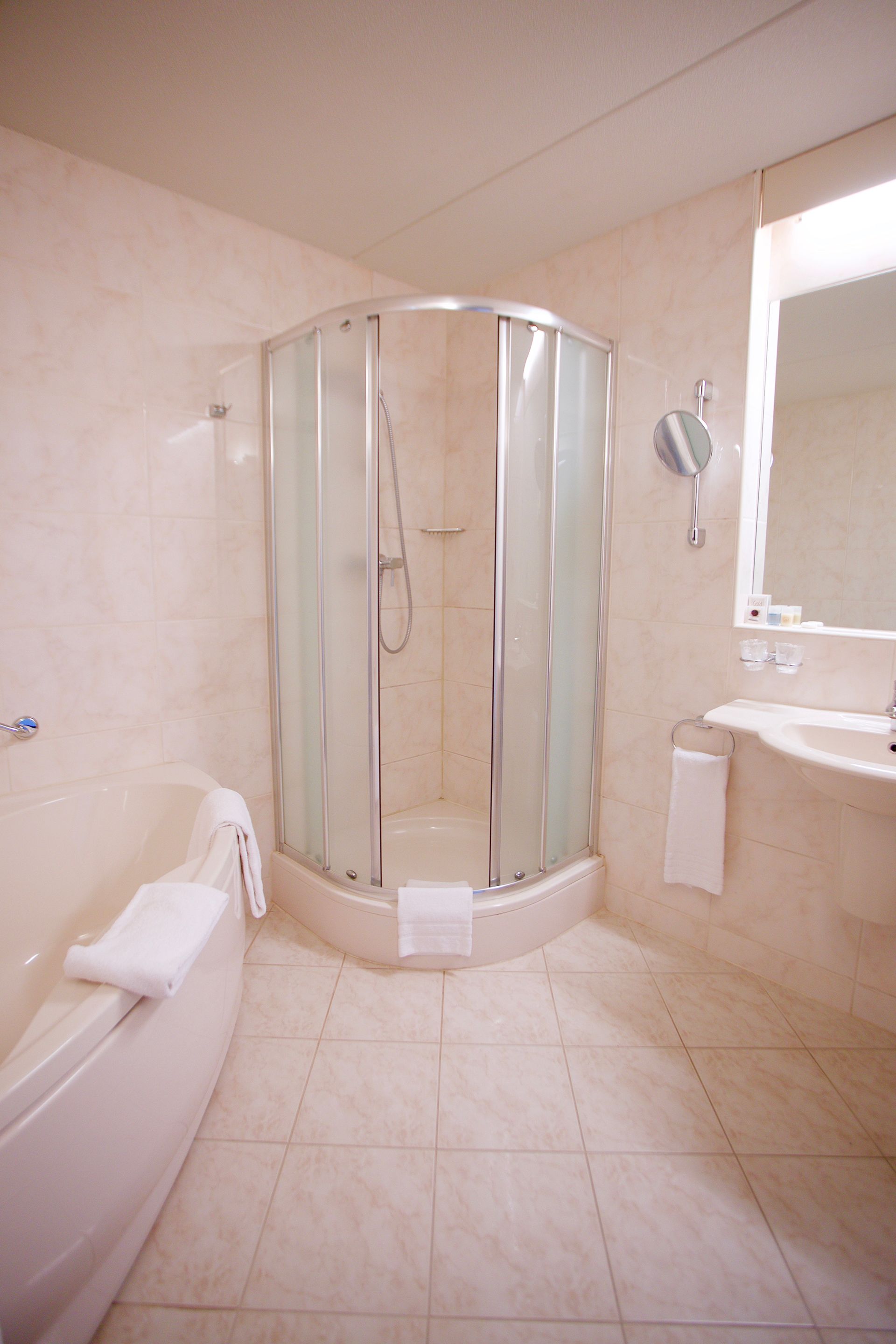 A modern bathroom with a glass-enclosed shower, a white bathtub, and a sink with a mirror.