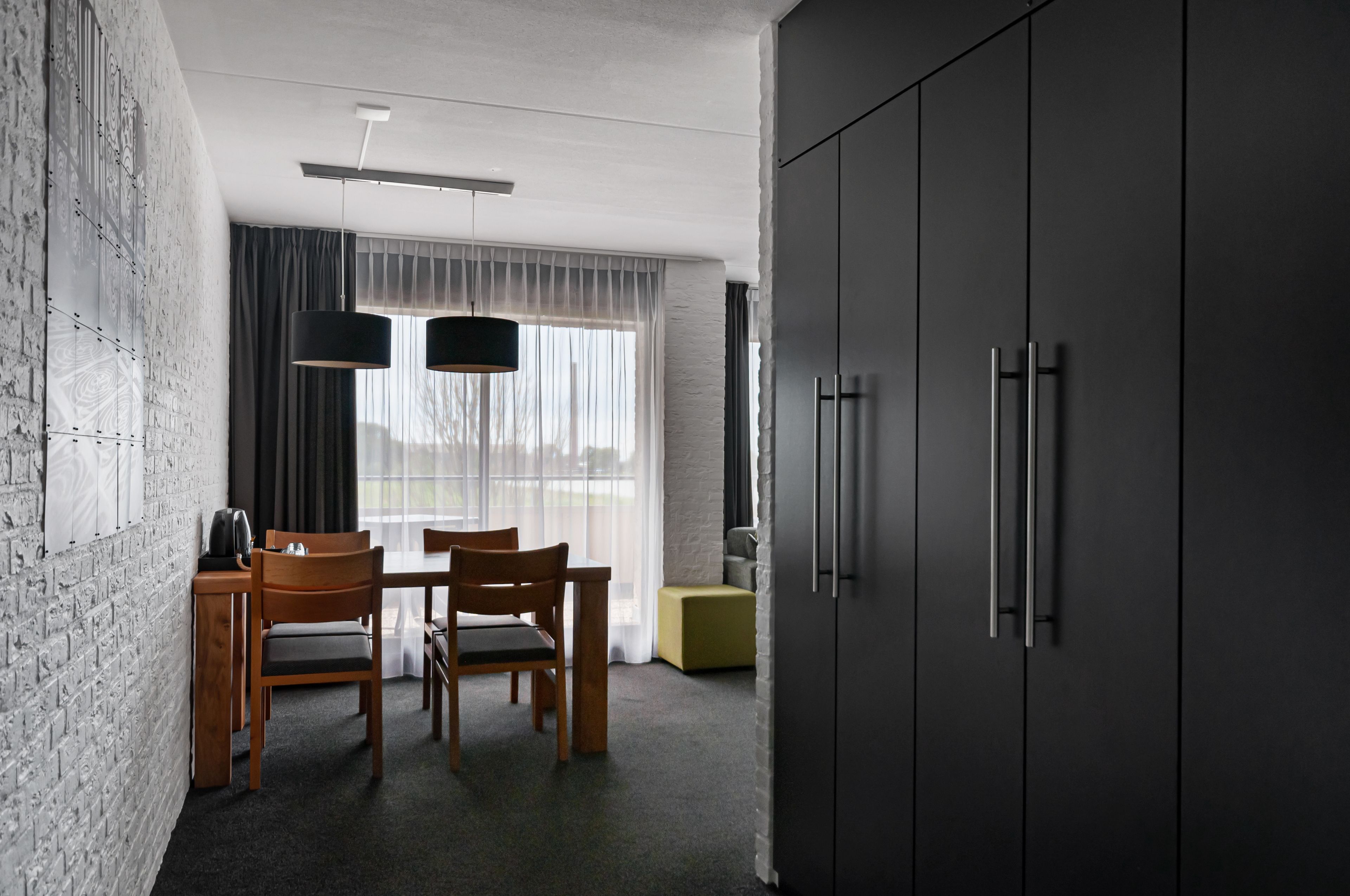 Habitación de hotel moderna con zona de comedor, un armario amplio y vistas al exterior.