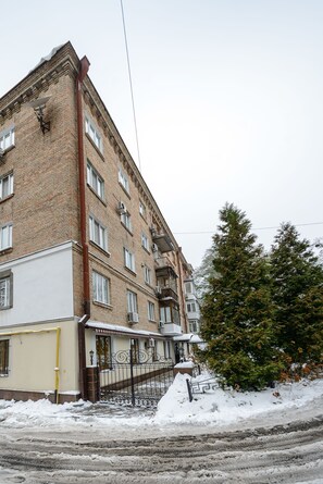 Un immeuble de plusieurs étages, construit en briques, dont le sol est recouvert de neige, et devant lequel se trouve un arbre.