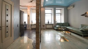 Un amplio salón con techo alto, un sofá verde, una mesa de comedor y una cocina visible a través de una puerta abierta.