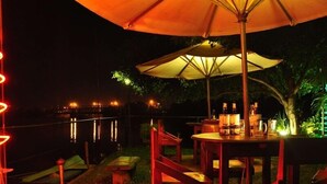 Een eethoek buiten met een tafel en stoelen onder een grote parasol, met uitzicht op een wateroppervlak.