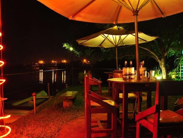 An outdoor dining area with a table and chairs under a large umbrella, overlooking a body of water.