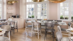A modern dining area with a central island, white chairs, and pendant lighting. - Hôtel Jeanne d'Arc Le Marais (Paris)