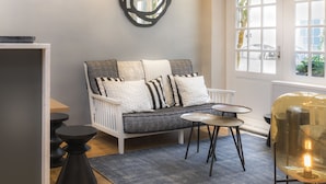 A modern living room with a white sofa, black and white cushions, a round coffee table, and a glass pendant light. - Hôtel Jeanne d'Arc Le Marais (Paris)