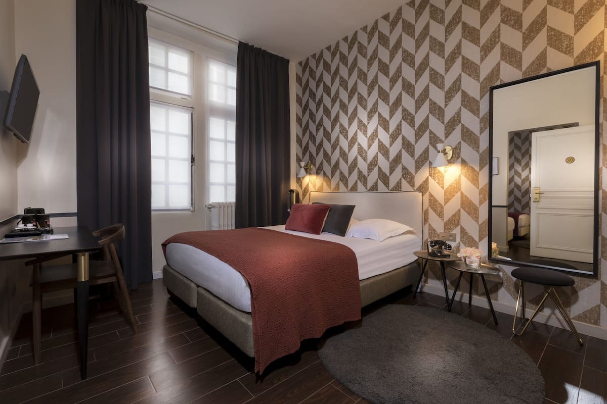 Hotellihuone, jossa on sänky, työpöytä, tuoli, peili ja ikkuna, jossa on verhot.