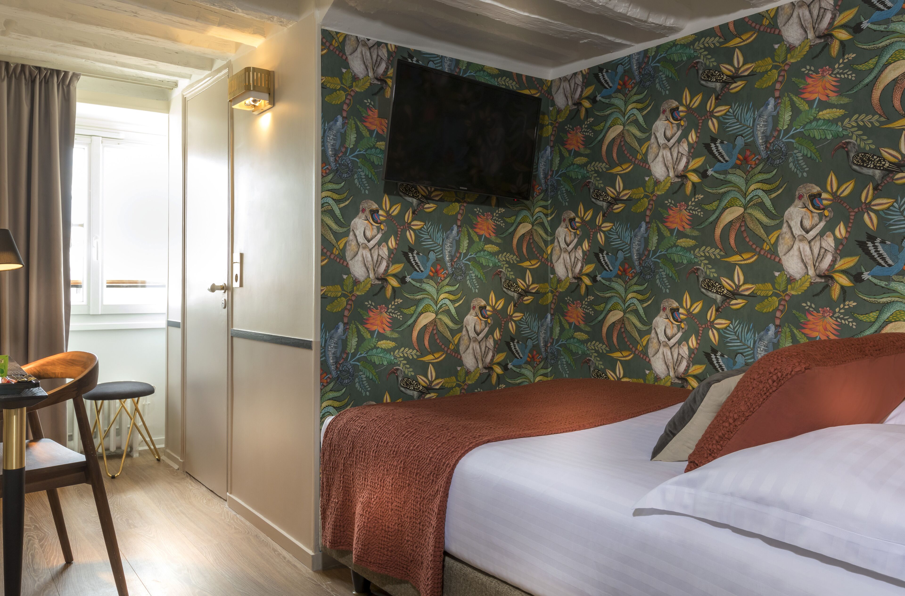 Ein Hotelzimmer mit einem Bett, einem Schreibtisch mit Stuhl, einem an der Wand befestigten Fernseher und einer Tür zu einem weiteren Raum.