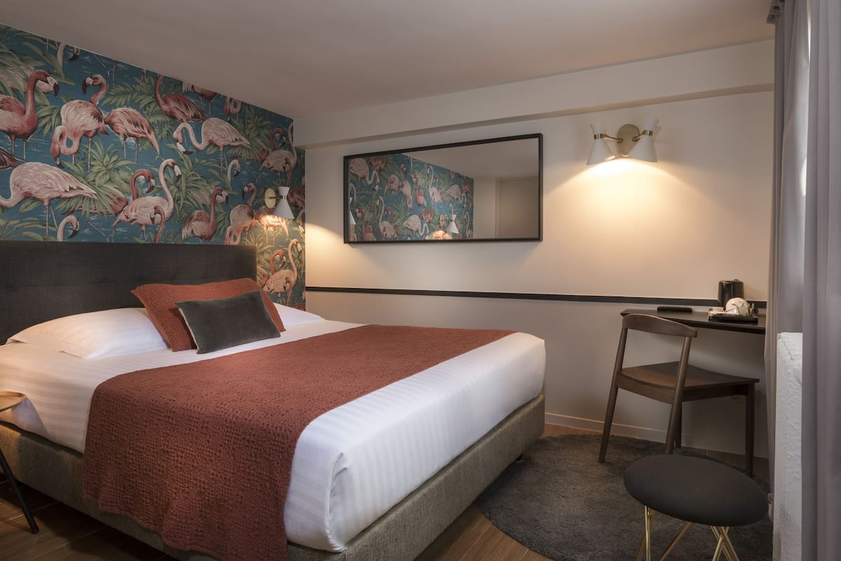 Hotellihuone, jossa on sänky, työpöytä, tuoli, peili ja seinä, joka on koristeltu trooppisella seinämaalauksella.