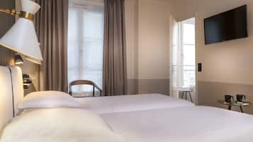 Una habitación de hotel con una cama grande, un televisor montado en la pared, una mesita con cafetera y una silla cerca de la ventana.