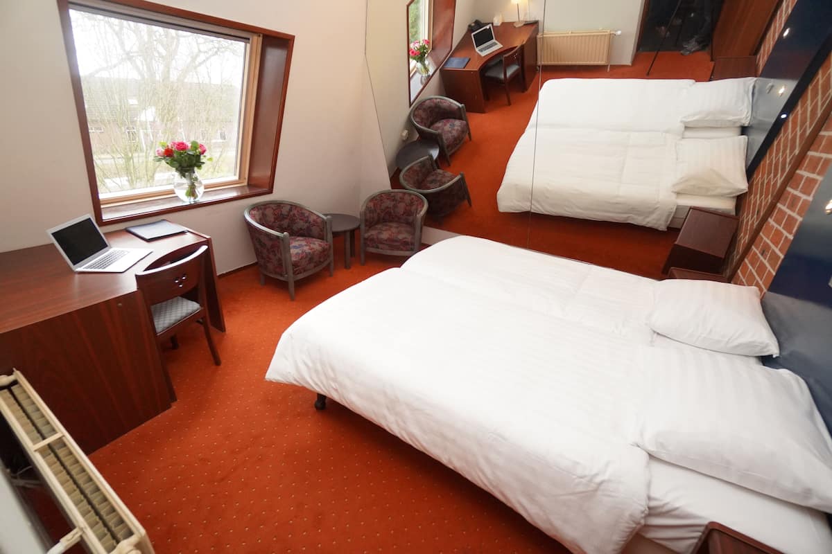 A hotel room with a large bed, a desk with a laptop, two armchairs, and a small table.