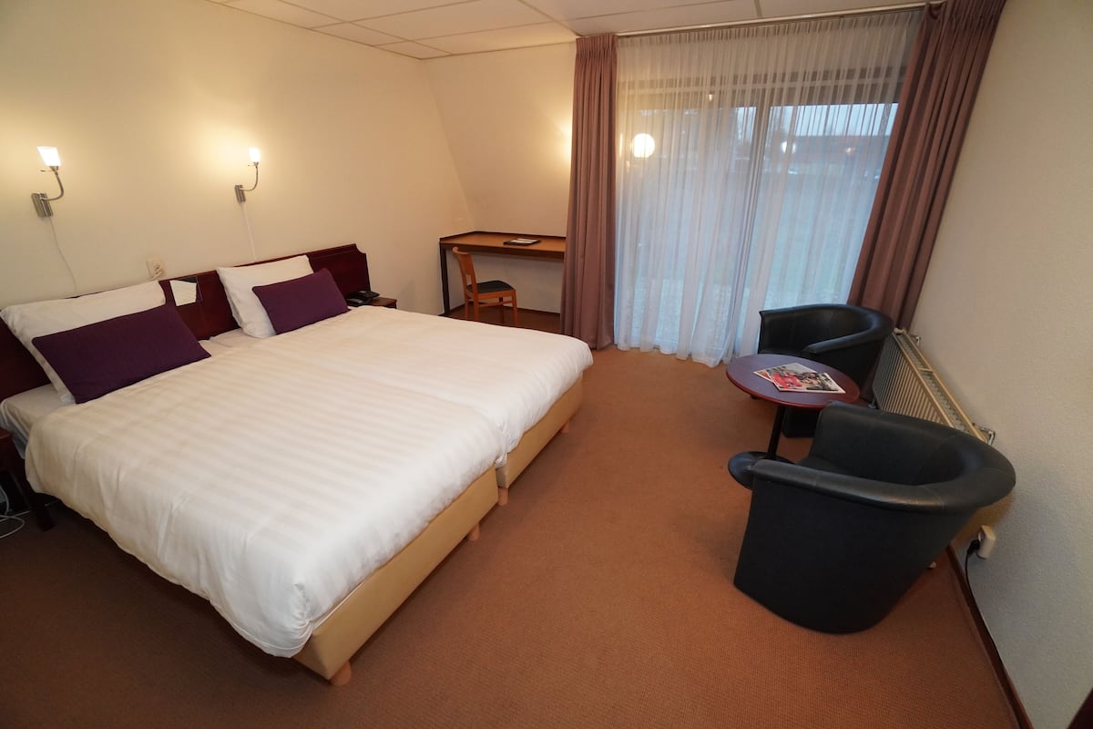 A hotel room with a large bed, a desk, a chair, and a small table.
